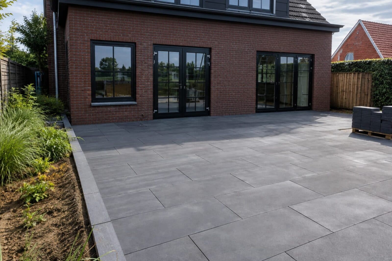 Opgeleverd terras van grijze betontegels langs de achtergevel, afgezet met opsluitbanden